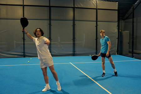 Two young men showcase their skills while playing padel with rackets on the court.