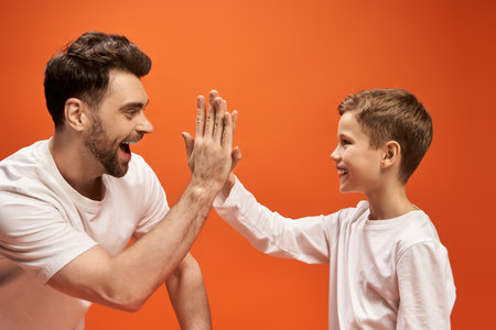 A father shares a joyful moment with his son, exchanging high fives against a vibrant backdrop.