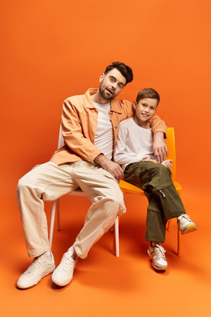 Father and son share a joyful moment against a bright orange backdrop.の写真素材