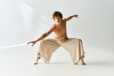 A young curly man showcases dynamic dance moves against a minimalist grey backdrop.の写真素材