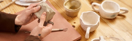 Handsome stylish man molds clay artfully in a pottery studio surrounded by finished works.