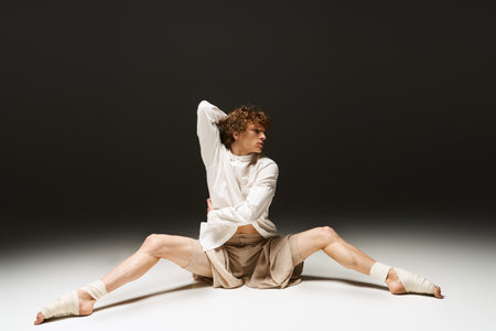 Young man with curly hair showcases athletic dance moves in a elegant studio environment.の写真素材
