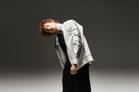 A young man with curly hair moves fluidly in a spacious dance studio, showcasing his skills.