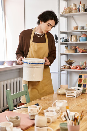 Handsome man wearing an apron carefully examines pottery materials in a vibrant studio