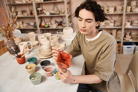 Handsome man focuses on crafting pottery, surrounded by an array of colorful materials and tools.の写真素材