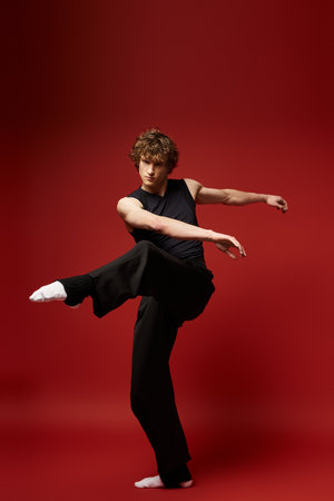 A young curly-haired man showcases his dancing skills against a bold red background.の写真素材