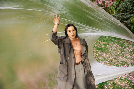 Young man embraces fashion in a grey trench coat while poses next to polyethylene, sustainability conceptの写真素材