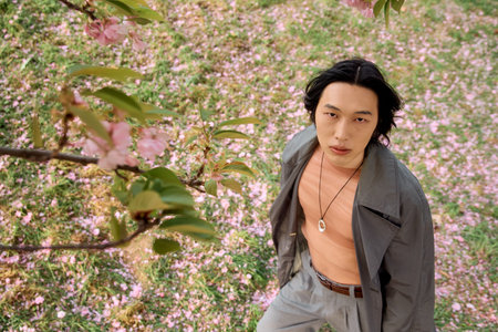 A young man in a fashionable grey outfit stands amidst blooming flowers, embracing tranquility.の写真素材