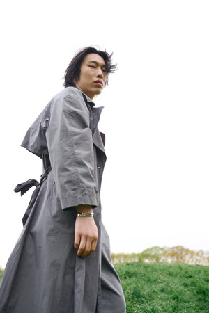 A young asian man showcases his stylish grey outfit while strolling through a serene park.の写真素材