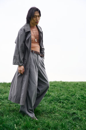 A young Asian man walks confidently in a stylish grey outfit while exploring a vibrant park.の写真素材