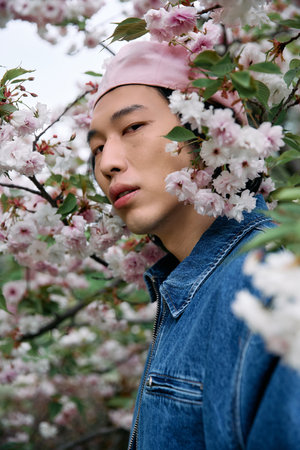 A young man in denim enjoys the serene park surrounded by blooming flowers.の写真素材