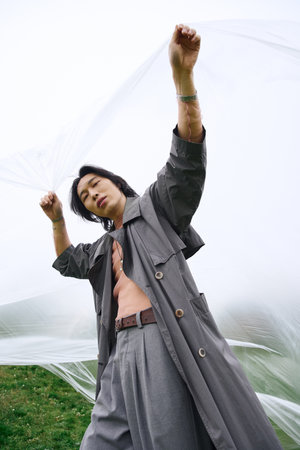 A young man showcases modern fashion in grey while enjoying a peaceful moment outdoors, holding polyethyleneの写真素材