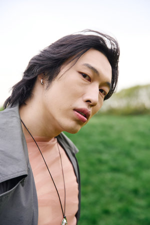 A stylish young Asian man wears a grey trench coat while enjoying a sunny day in the park.の写真素材