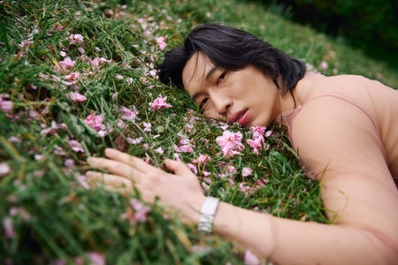 A young asian man rests on grass surrounded by flowersの写真素材