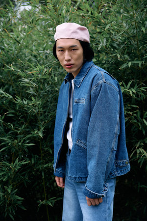 A young asian man dressed in a trendy denim outfit poses confidently among greenery in a park.の写真素材