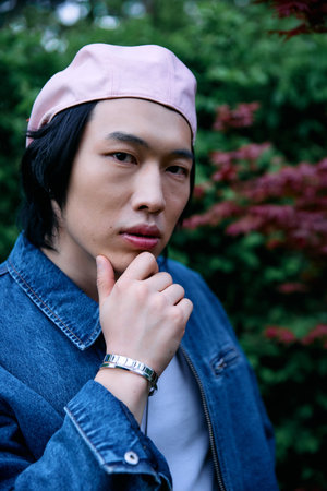 Young asian man poses confidently in a denim outfit surrounded by greenery in the park.の写真素材
