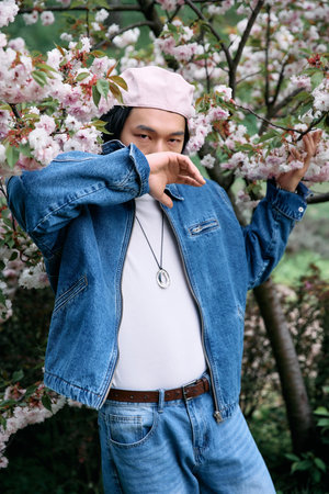 A young man dressed in trendy denim enjoys the beauty of nature in a park filled with blossoms.の写真素材