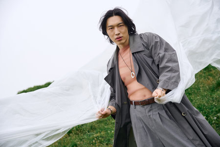 A young Asian man models a grey outfit, playfully engaging with polyethyleneの写真素材