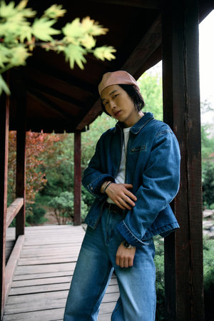 A young asian man showcases his trendy denim outfit while relaxing in a beautiful park.の写真素材