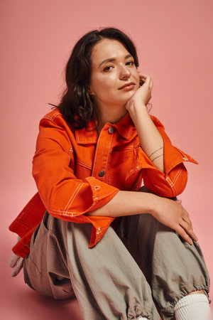 A young beautiful woman poses thoughtfully, highlighting her chic outfit amidst a colorful setting.