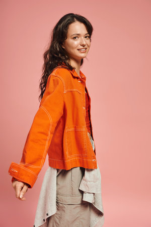 A fashionable young woman showcases her bright orange jacket with a charming smile, radiating style.の写真素材