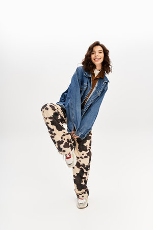 Young woman in a trendy outfit, featuring cow print pants, poses playfully in a studio setting.の写真素材