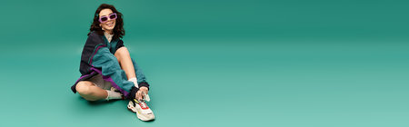 Young woman in fashionable sporty attire relaxes on the floor with a playful smile, bannerの写真素材