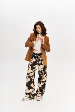 A confident young woman poses in trendy cow print pants against a grey backdrop.
