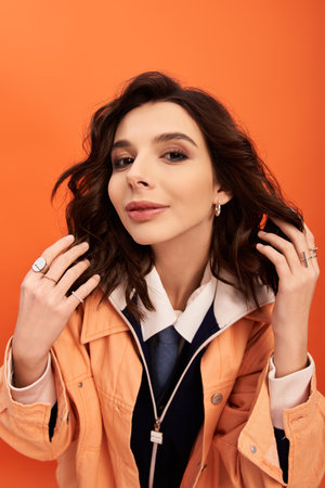 A young woman in a trendy outfit poses confidently against a bright orange backdrop.の写真素材
