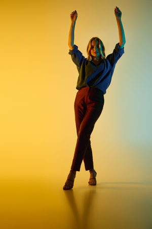 A young woman wearing fashionable clothing strikes a confident pose under bright lights.の写真素材