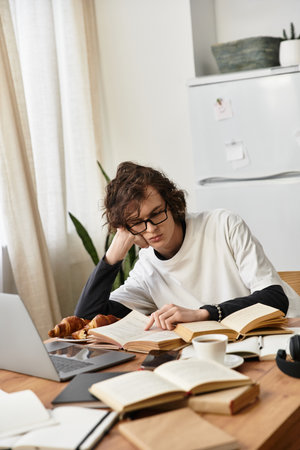 A cozy young man studies at home, surrounded by books and a laptop, exuding comfort.の写真素材