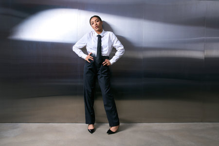 Sophisticated individual confidently poses in tailored attire against a sleek metallic background.の写真素材