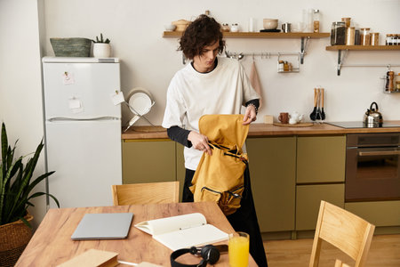A young man dressed comfortably prepares his backpack in a modern kitchen filled with warmth.の写真素材