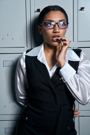 Young woman in chic attire contemplates while leaning against lockers with poise and grace.の写真素材