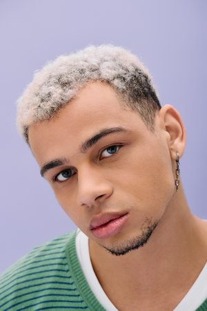 A young african american man proudly poses in a trendy outfit with his dyed hair styled creatively.