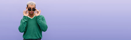 A stylish young Black man with dyed hair poses confidently against a purple background, banner