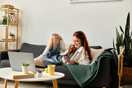 Beautiful woman with red hair relaxes on a couch while using her laptop in a modern living space.