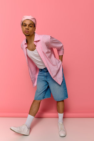 A young african american man poses confidently in a checkered shirt and beret, exuding style.