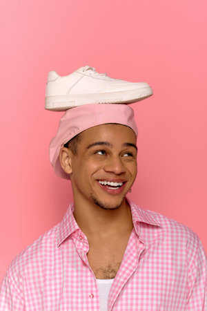 A young african american man with a cheerful expression balances a sneaker on his beret.の写真素材