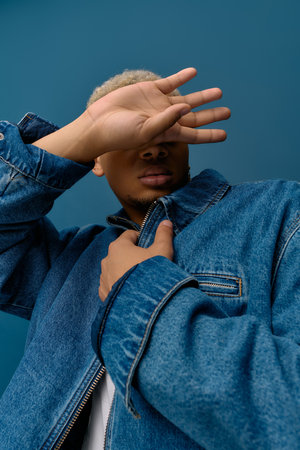 A stylish young Black man in a denim jacket poses against a vibrant background.