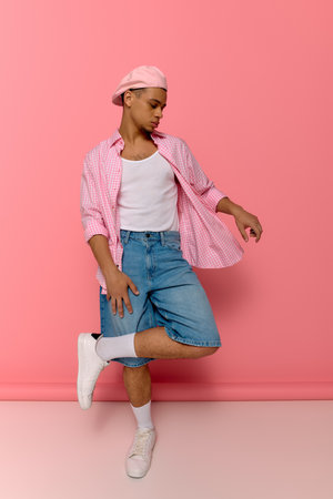 A stylish young Black man poses confidently on a bright pink background in a chic beret and shirt.の写真素材