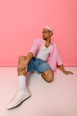 A young African American man showcases his style on a bright pink background, exuding creativity.の写真素材