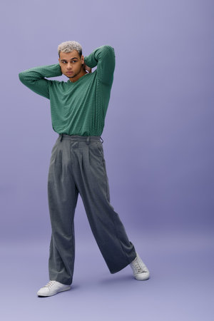 A young African American man poses confidently in stylish attire with a bold purple background.