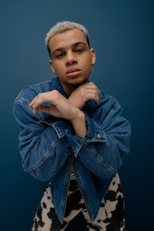 A confident young African American man poses with crossed arms in a trendy denim jacket.