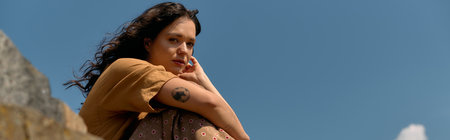A young woman with curly hair relaxes outdoors in a stylish summer outfit, embracing the sun, bannerの写真素材