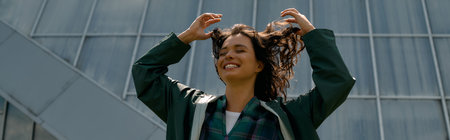 A young woman with curly hair playfully poses in a stylish raincoat, bannerの写真素材
