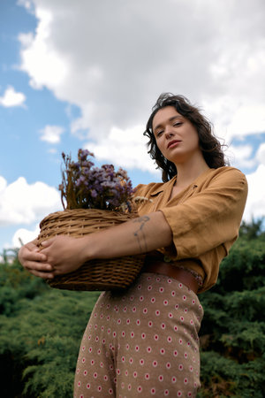 A confident young woman with curly hair enjoys summer outdoors, posing with flowers.の写真素材