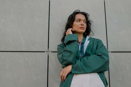 A stylish young woman poses confidently in a trendy raincoat outdoors, embracing summer vibes.の写真素材