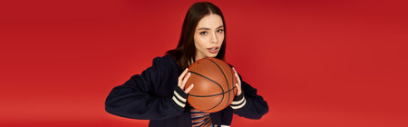 Young woman demonstrates confidence while posing with a basketball against a bold red backdrop.の写真素材