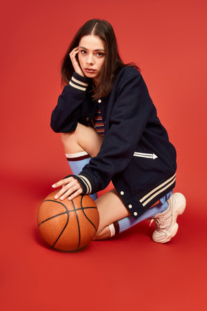 Vibrant and fashionable young woman squats with a basketball, exuding confidence and style.の写真素材